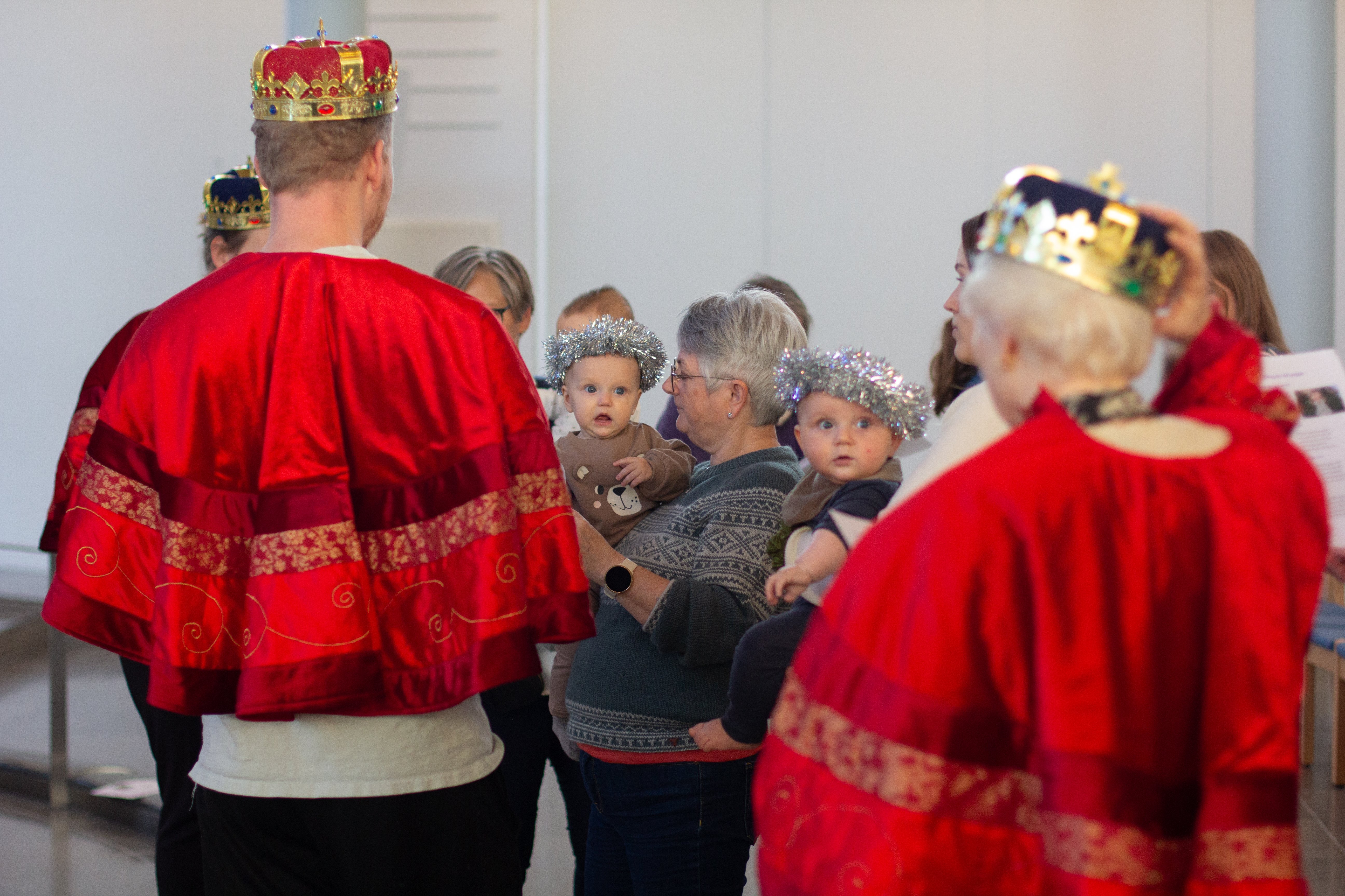 Vise menn viser frem gavene til babyene som har glitterkrans på hodet. De ser forundret ut.