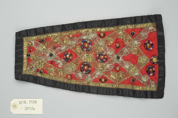 Gammel d&aring;pssmekke fra Vestlandet, r&oslash;d med fargerike perler og gullblonder. Foto: Nordfjord folkemuseum