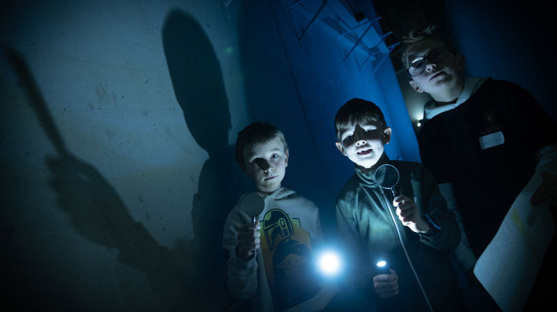 Synstolkning: tre barn med lommelykter på vei til kirketårnet.