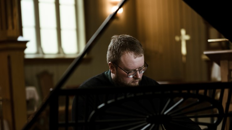 En kantor som sitter ved et orgel i et kirkerom.