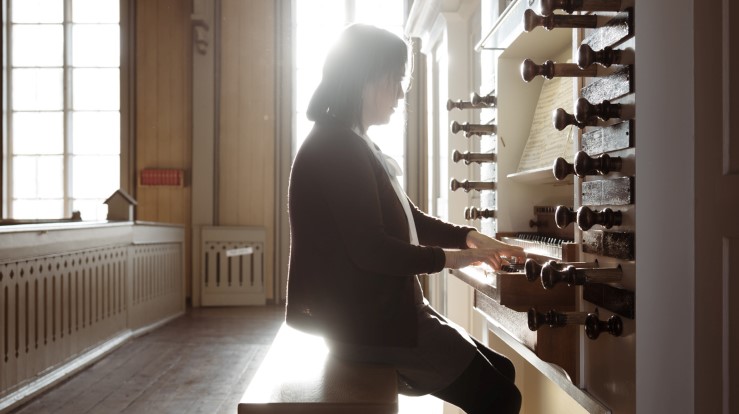 Kantor sitter ved orgelet og spiller. Lyset fra vinduet skinner sterkt.