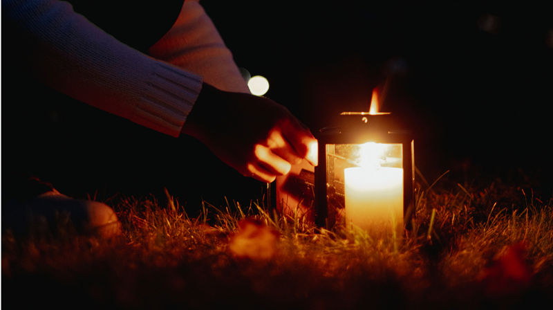 En hånd tenner en lykt ute. Det er mørkt og kveld.