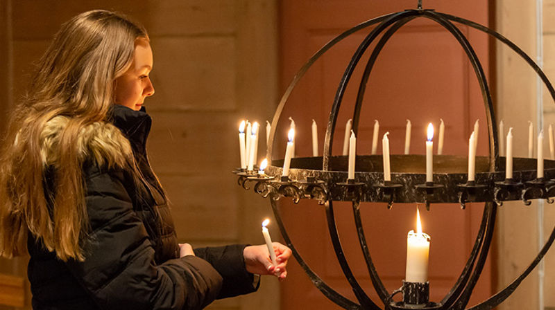 Ei ung jente med ytterjakken på tenner lys i kirken