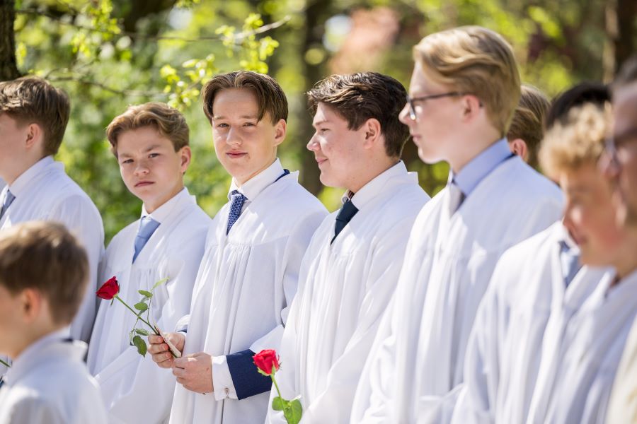 Det er konfirmasjon i kirken. En gjeng konfirmanter i konfirmantkapper som ser opp på kamera.