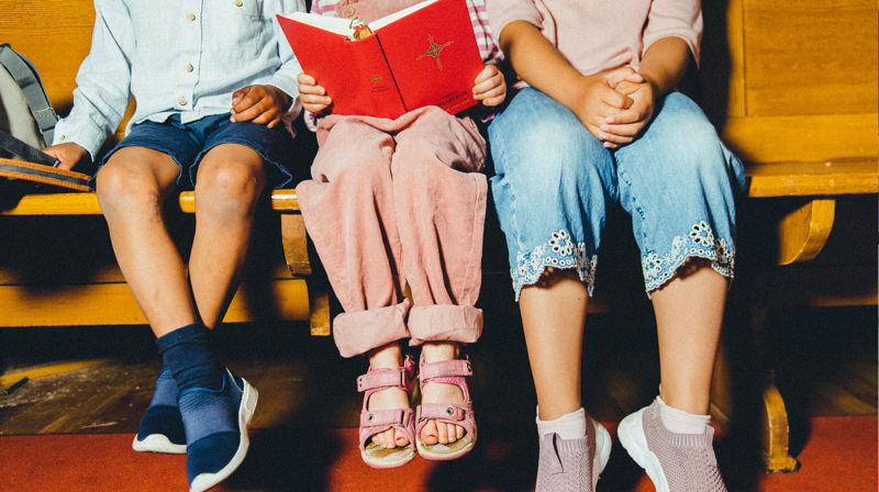 Tre barn sitter tett og ser i salmeboka