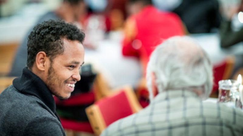 En ung mann smiler og har en god samtale med en eldre mann. Språkkafé og kirkekaffe er flotte fellesskap i kirken.