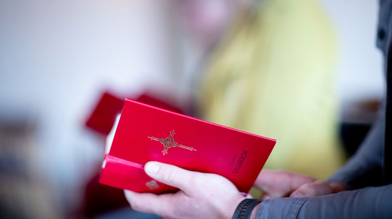 Mann holder en oppslått salmebok.