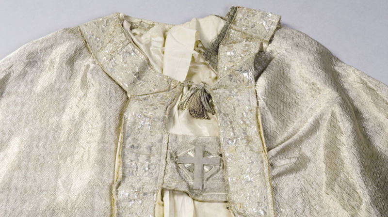 Kåpen fra 1864 har sølvkniplinger langs kantene, og et sølvkors på spennet.