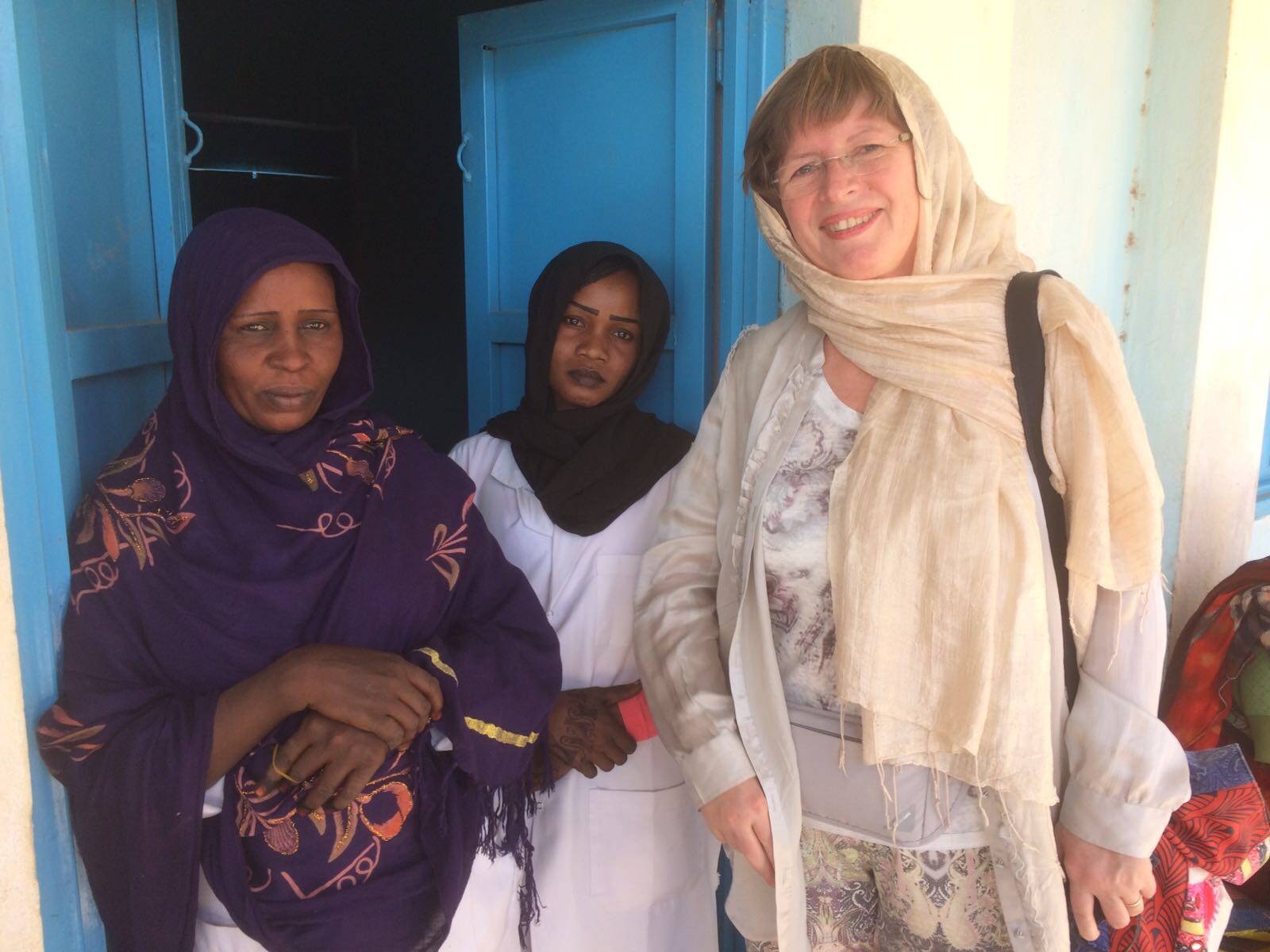 Ingeborg i Darfur utenfor en fødestue, sammen med søster og mor til en fødende kvinne. De har båret med seg 8 jerrykanner med vann til fødselen fordi fødestuen ikke hadde innlagt vann