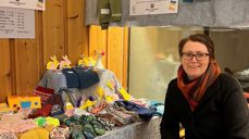På bildet sitter Øygunn Østhagen foran fasteaksjonsamarkedet i 2022. På bordet ligger blant annet flotte strikkede votter, luer, gensere og forskjellig påskepynt laget av barn og voksne. Foto og tekst: Jenny Marie Ågedal.
