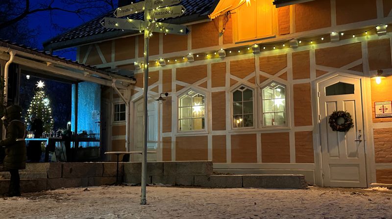 Bilde av Pilegrimssenteret i Oslo, utenfor inngangsdøren. Et veiskilt dekket i lyslenker i front av bildet. Bygget har en lyslenke og advensstjerne hengt opp til pynt,