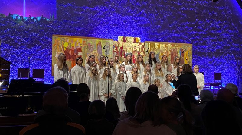 Korsangere i hvite kapper foran Holmen kirkes altertavle og blå fondvegg.