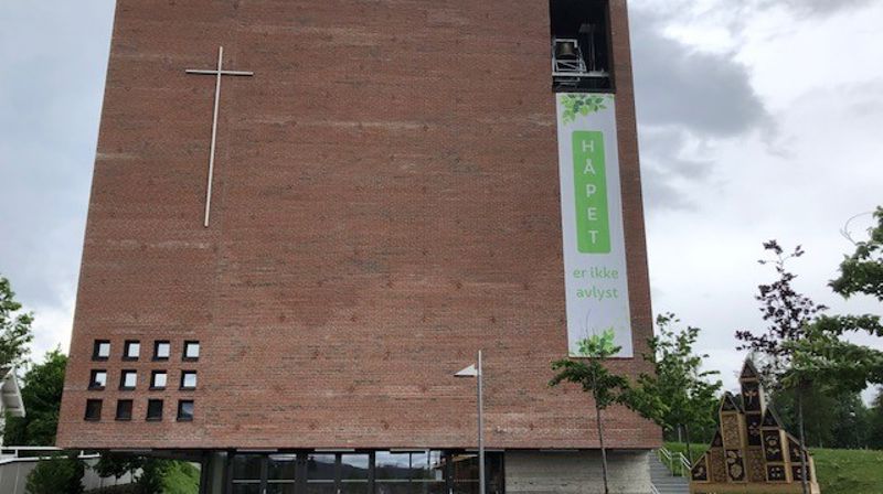 Fronten av Teglen vender ut mot torget på Spikkestad. Øverst til høyre kan vi se tårnrommet der det henger tre kirkeklokker.