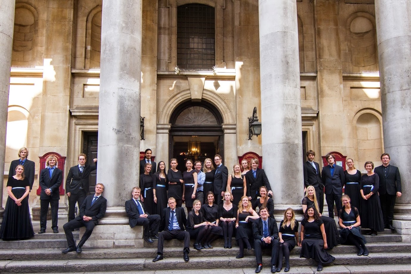 St.Sunniva kammerkor på tur. Oppstilt i trapper utenfor offentlig bygning.