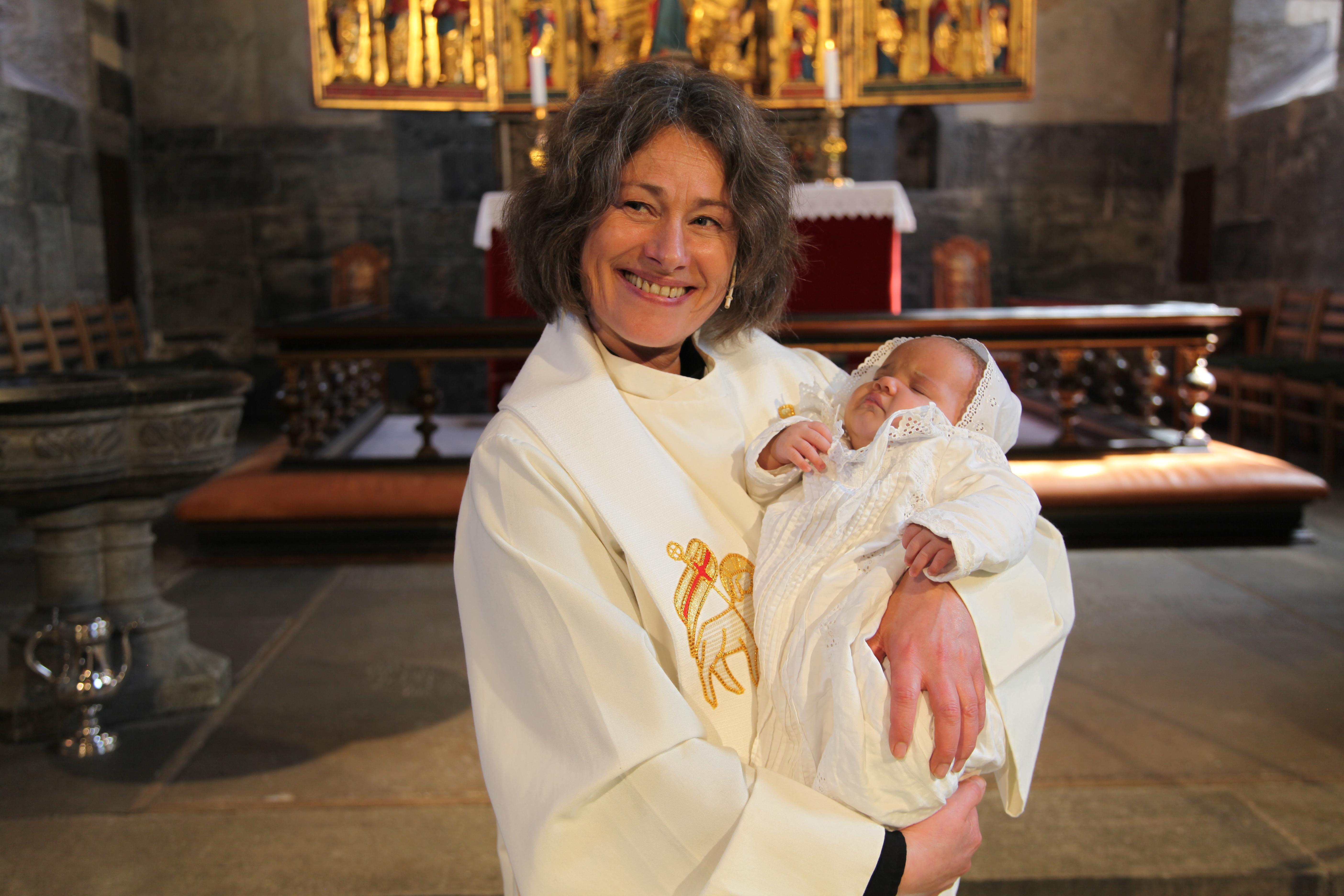 Prest Hildegunn Isaksen som holder dåpsbarn i Mariakirken.