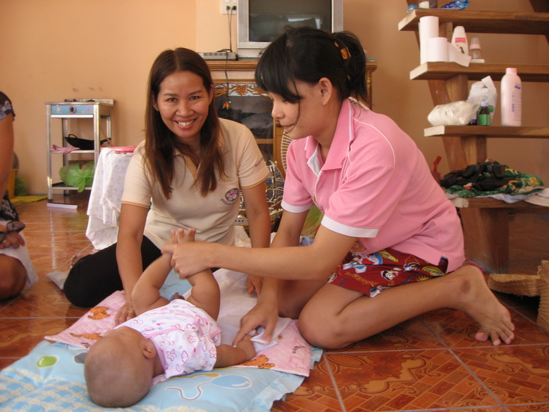 En nybakt mamma steller babyen sin sammen med en ansatt ved Nådehjemmet, som ser på kameraet og smiler.