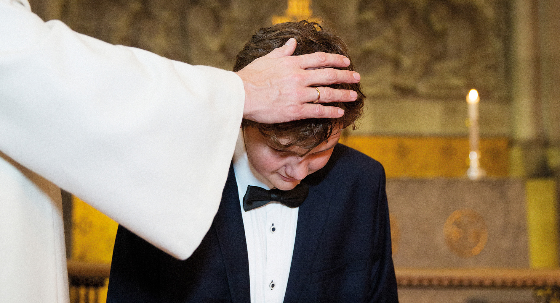 En ung gutt blir døpt. Presten har hånden på hodet hans. Han blir nå medlem i kirken.