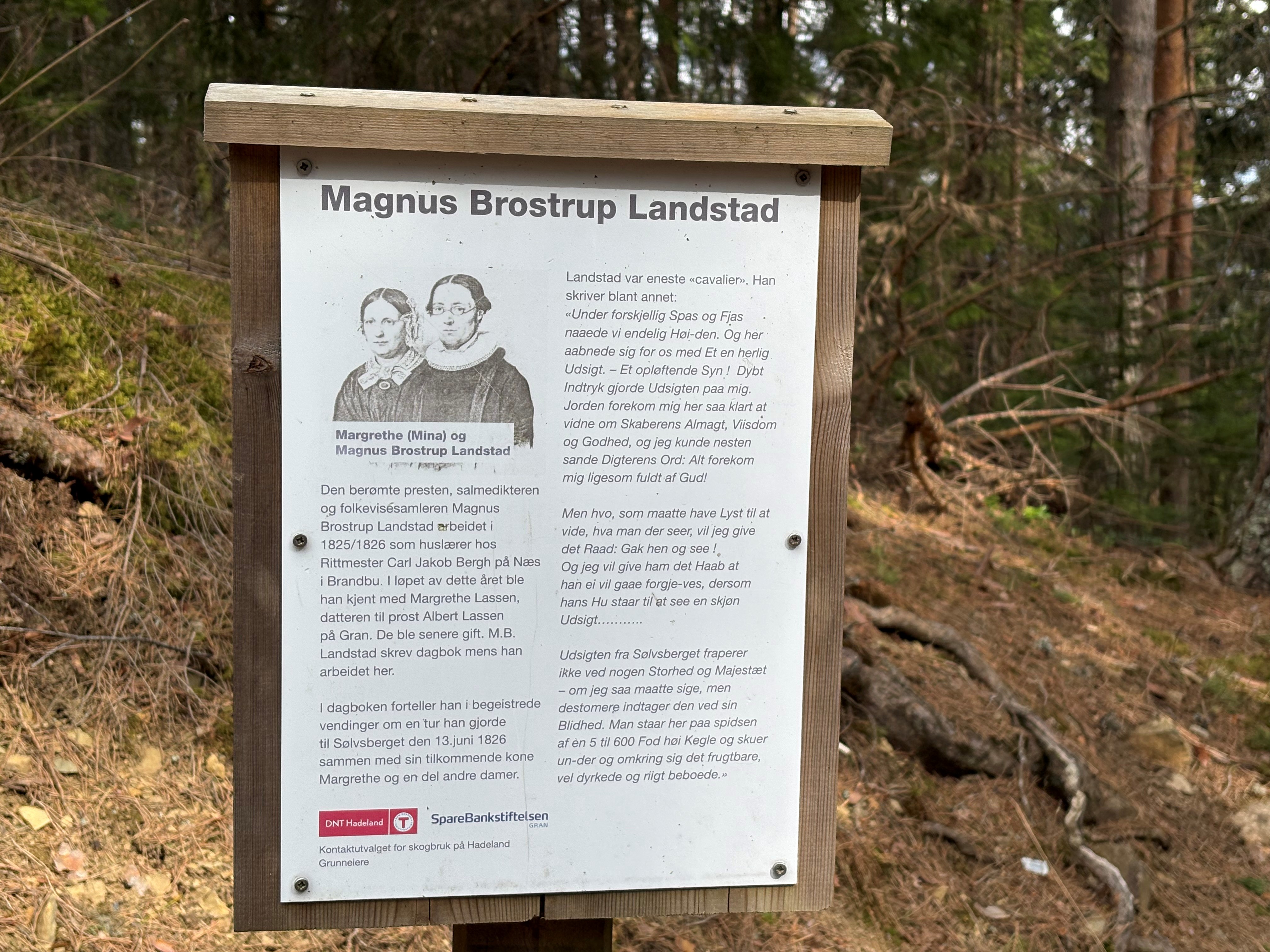 På vegen opp til Sølvsberget, finner du denne informasjonsplakaten til DNT Hadeland, som forteljer om Landstad og om turen til Sølvsberget som Magnus og Mina gjorde i 1826. Foto: Kirken i Gran/Inger S. Haug.