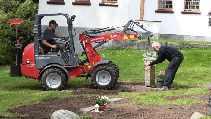 Ferdig: Mandag ble de siste gravsteinene løftet på plass etter sju års arbeid med cirka 2.500 gravsteiner på kommunens kirkegårder. Her ser vi gravplass- og kirkebyggsjef Bjørn Undheim med steinen og Helge Flaath i traktoren.