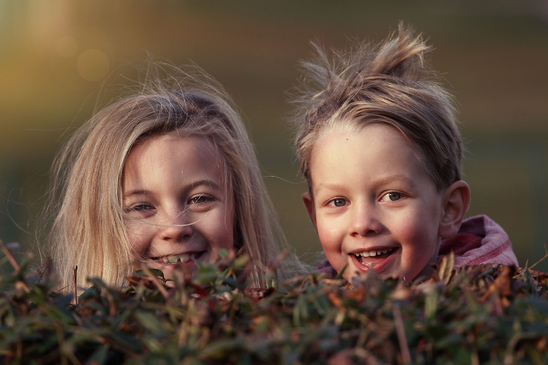 På bildet ser vi to små barn som titter opp bak vegetasjon. Vi ser bare hodene deres. Foto: Lenka Fortelna fra Pixabay