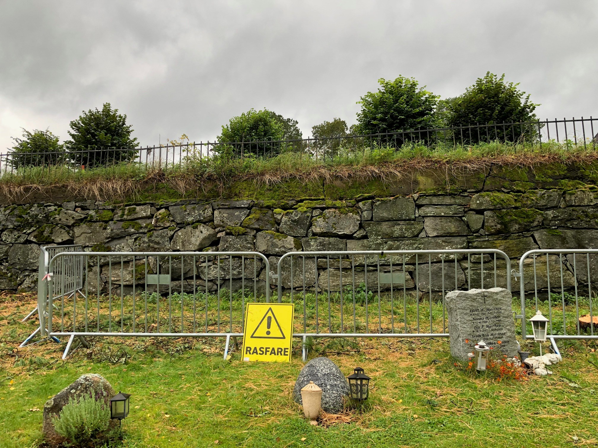 Støttemur med sikringshekk og skilt Rasfare. 