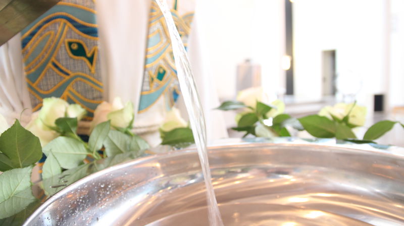 Presten heller vann oppi døpefonten, hvite roser er pyntet med rund sølvfatet.