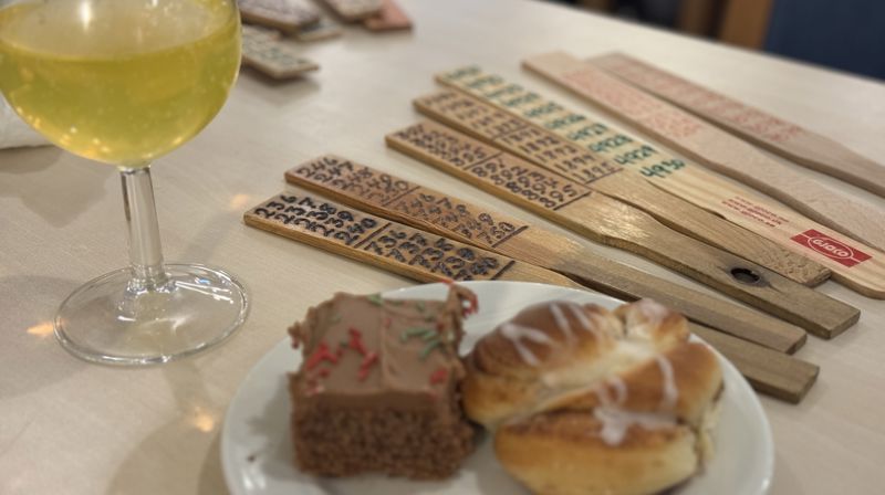 På et bord står et glass meed gul drikke, et fat med et kakestykke og en bolle og flere årer til basar