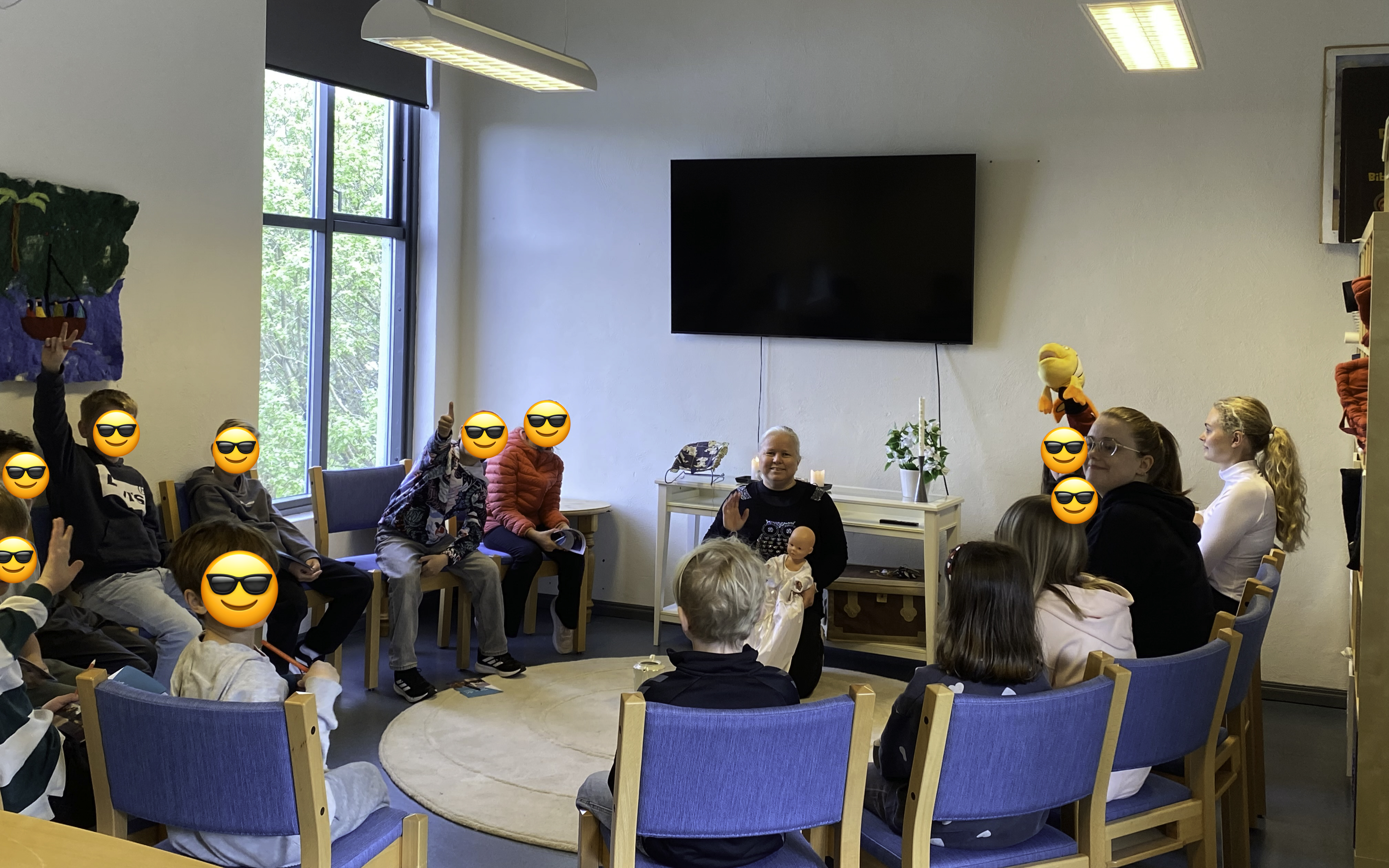 Barn og l&aelig;rere sitter i en halvsirkel, ansiktene til barna er gjemt med en emoji med solbriller
