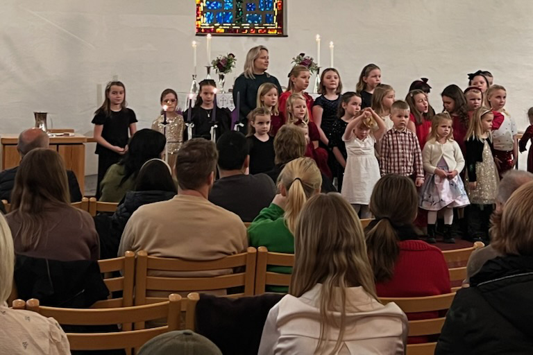 Et barnekor st&aring;r framme i kyrkja og syng til publikum