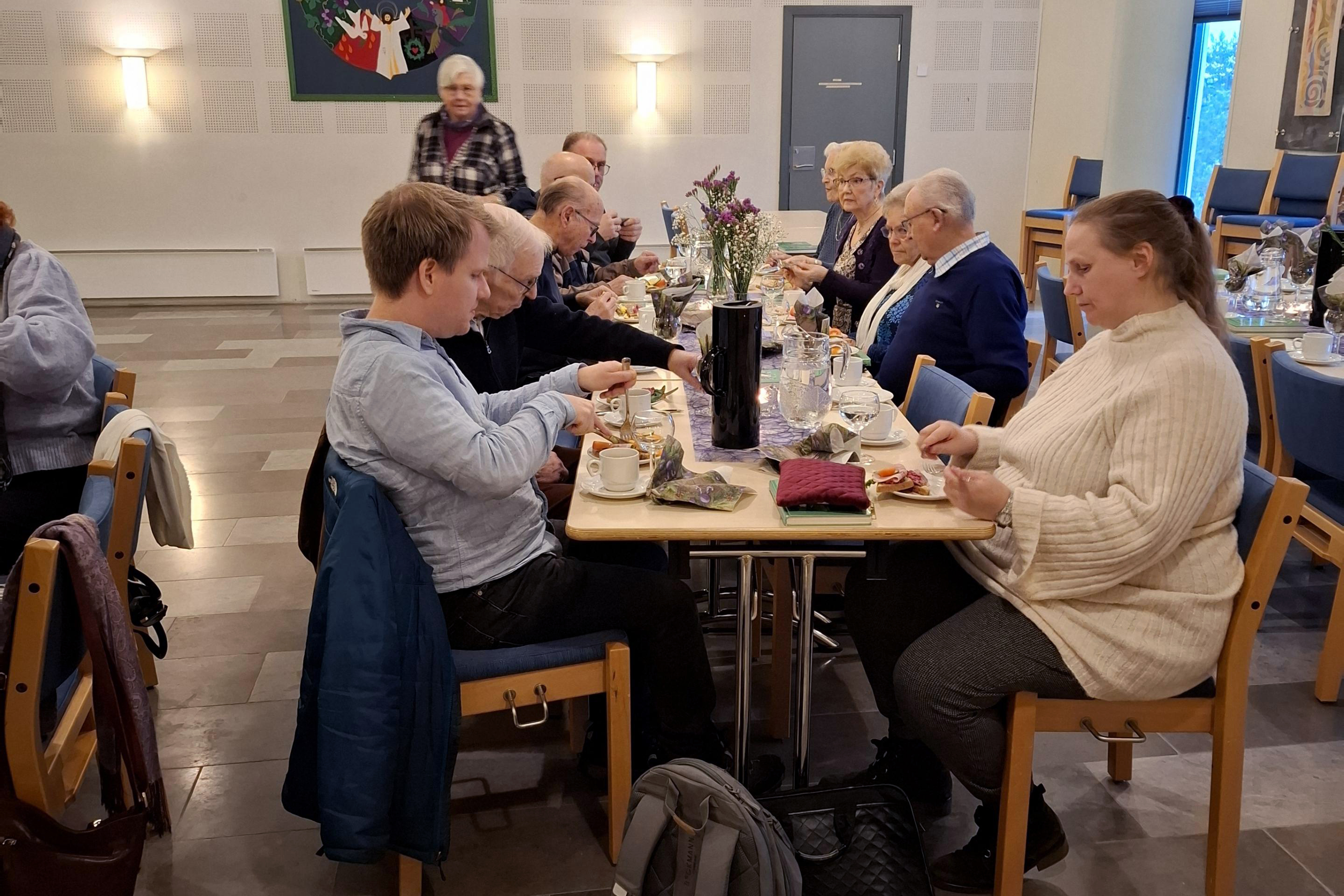 Flere mennesker sitter ved et lenger bord og spiser mat