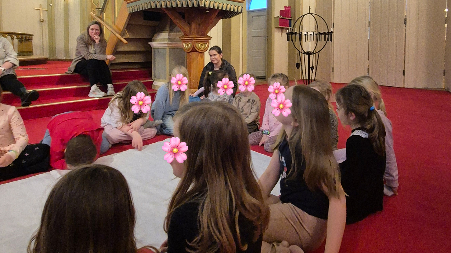 Barn sitter rundt et lang rull hvitt papir, fjesene er skjult med en blomster emoji.