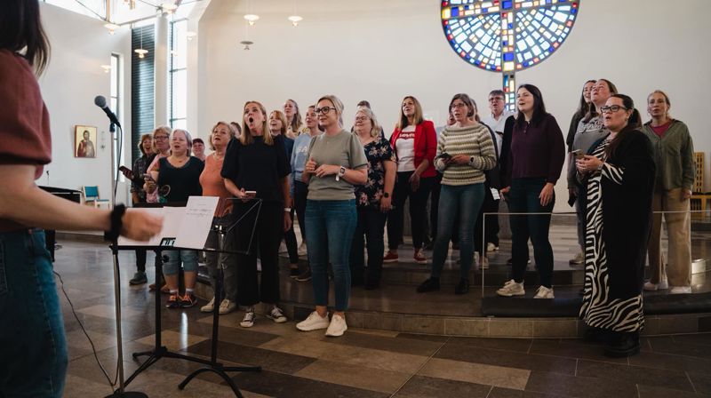 Gospelkoret str oppstilt framme i kyrkja og øver med ditigenten