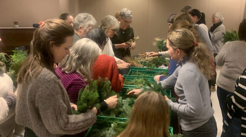 Mennesker går langs eit bord og plukker opp ting og greinar dei kan lage kransar med