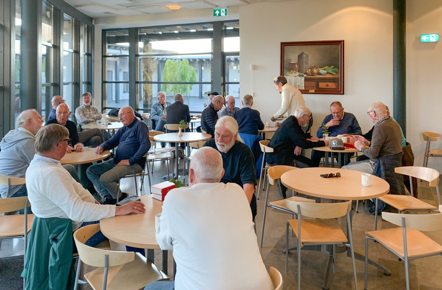 Menn sitter rundt flere småbord og prater sammen