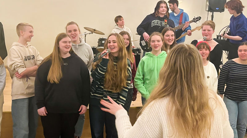Ungdommer som synger i kor, med et band i bakgrunnen
