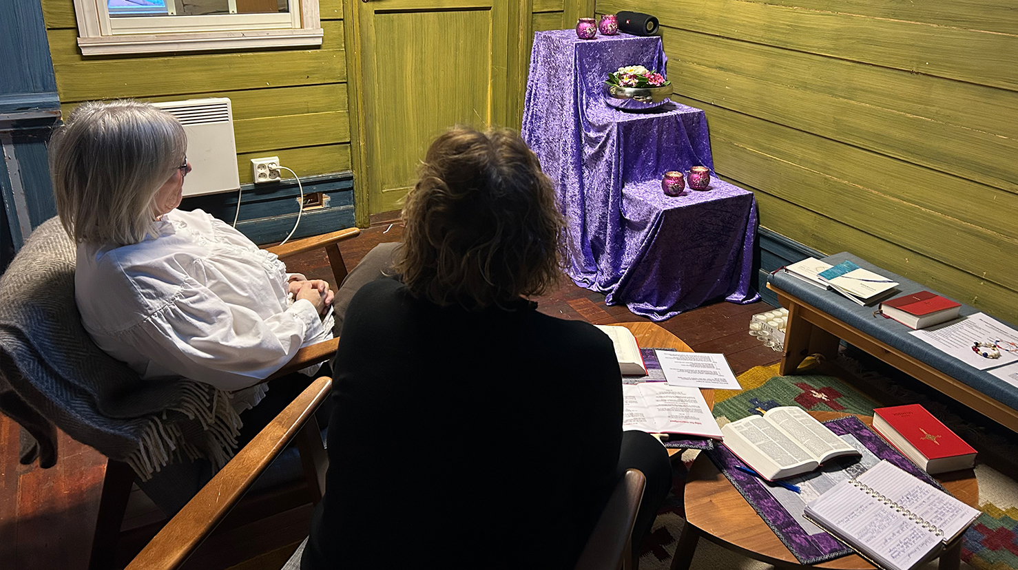 To damer sitter på hver sin stol inne i et rom og ber