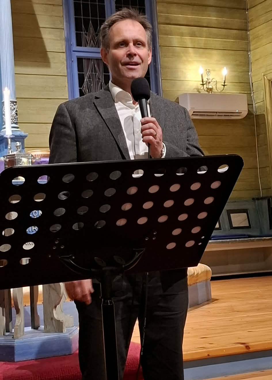 En mann står fremme i en kirke og synger i mikrofon