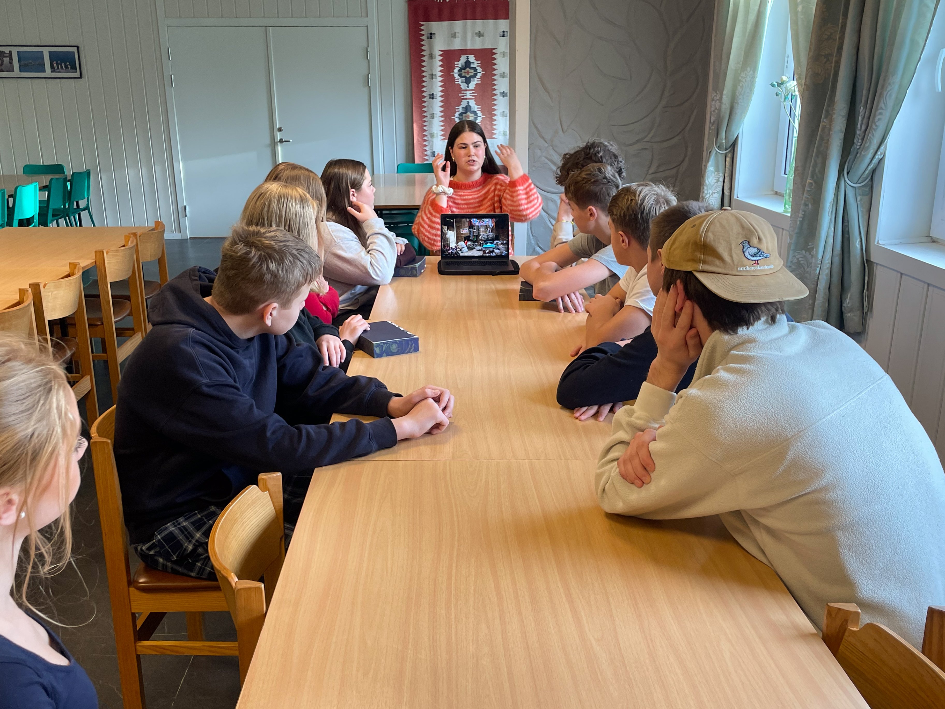 Ungdommer sitter langs et bord og ser og hører på en som forteller 