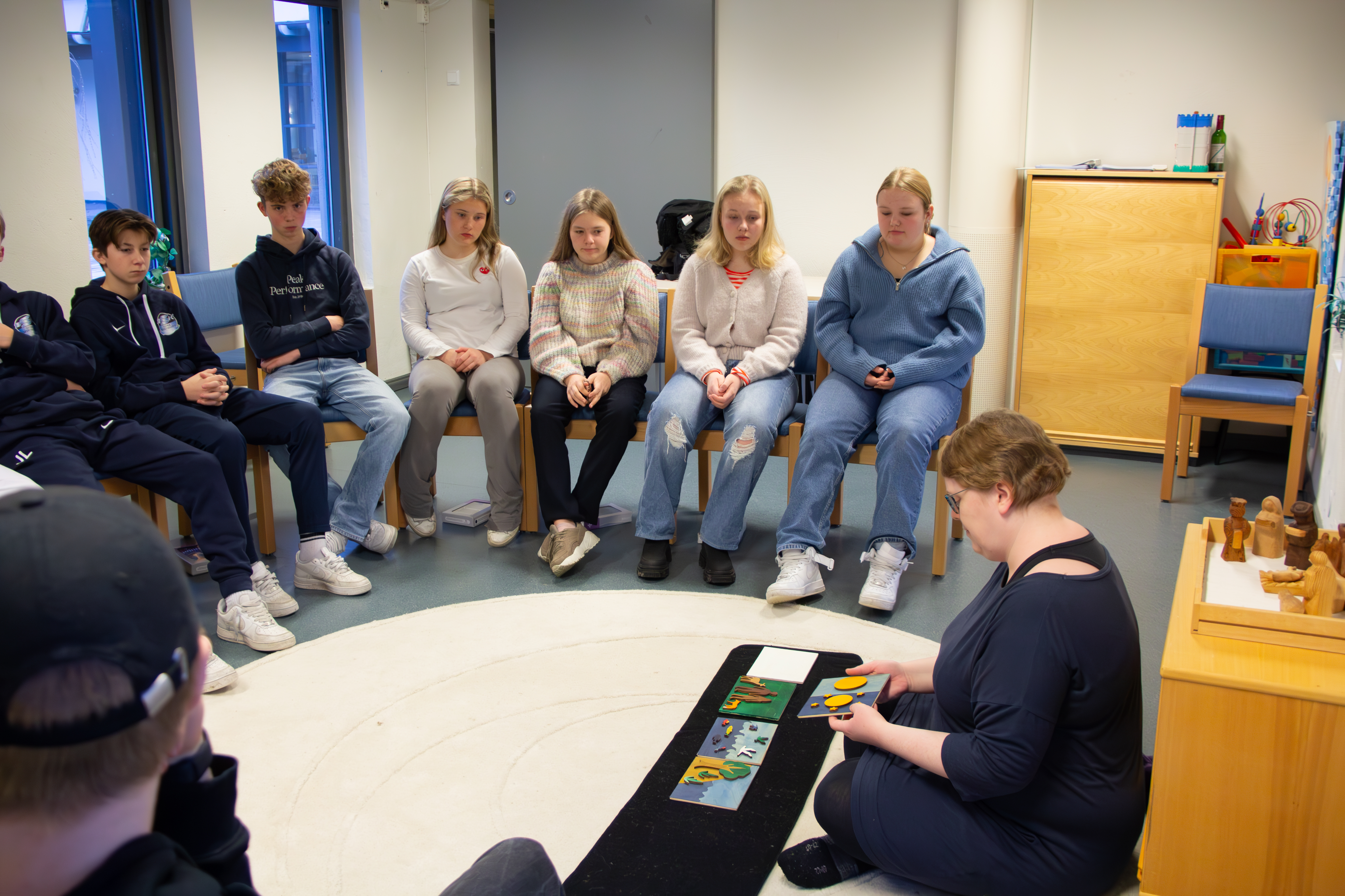 Ungdommer sitter i en halvsirkel og ser på en konfirmantlærer som viser frem en historie