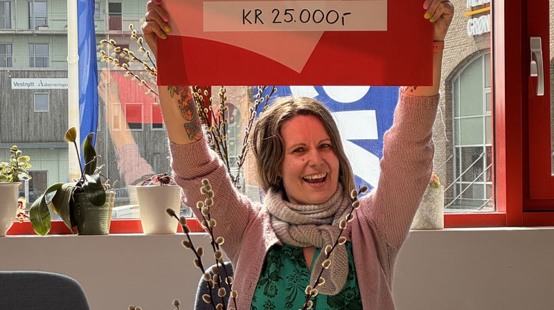 En dame holder opp en stor rød gavesjekk over hodet og smiler