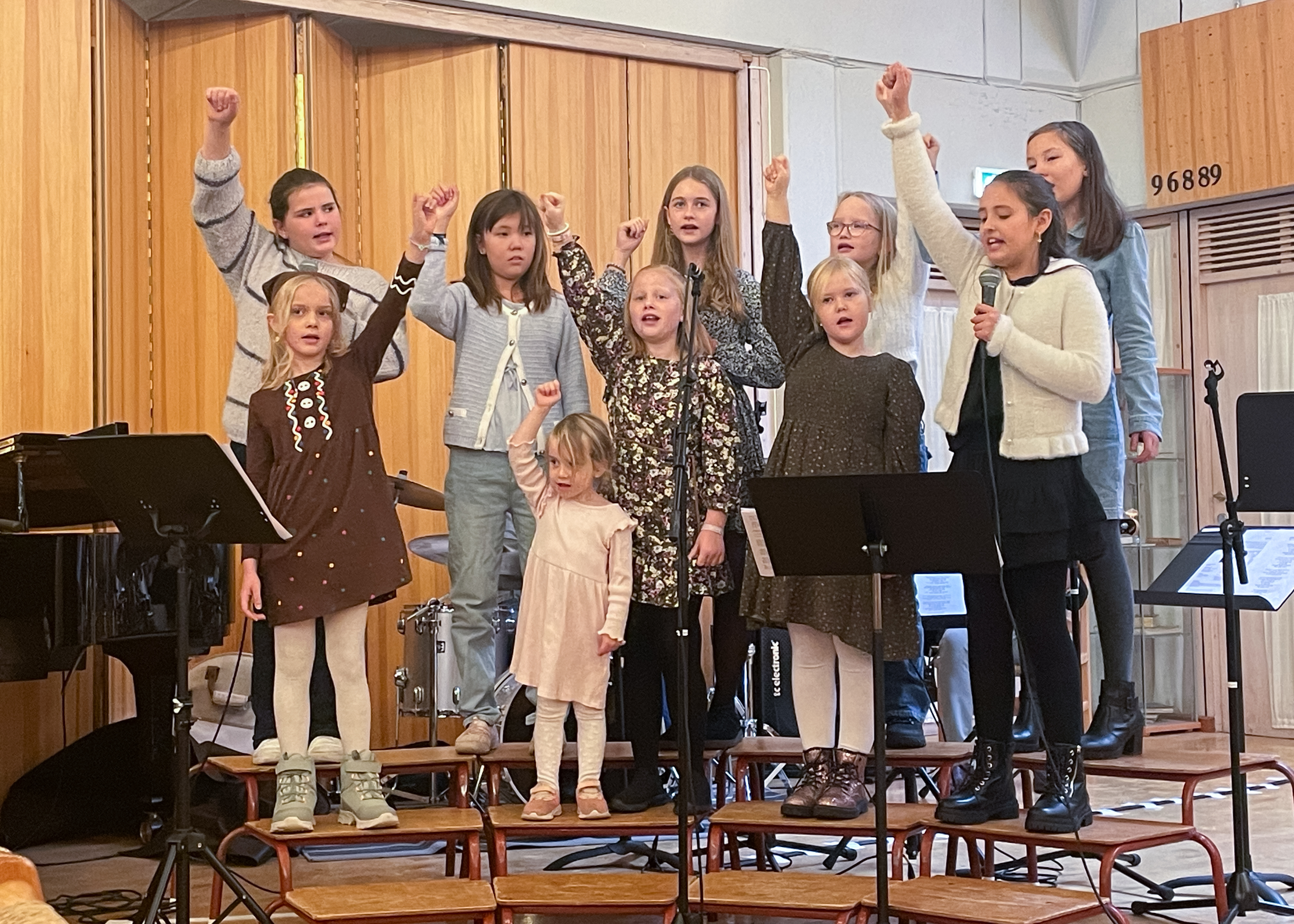 barne- og tweenskoret står på korkrakker, synger og lager bevegelser. de er fint kledd