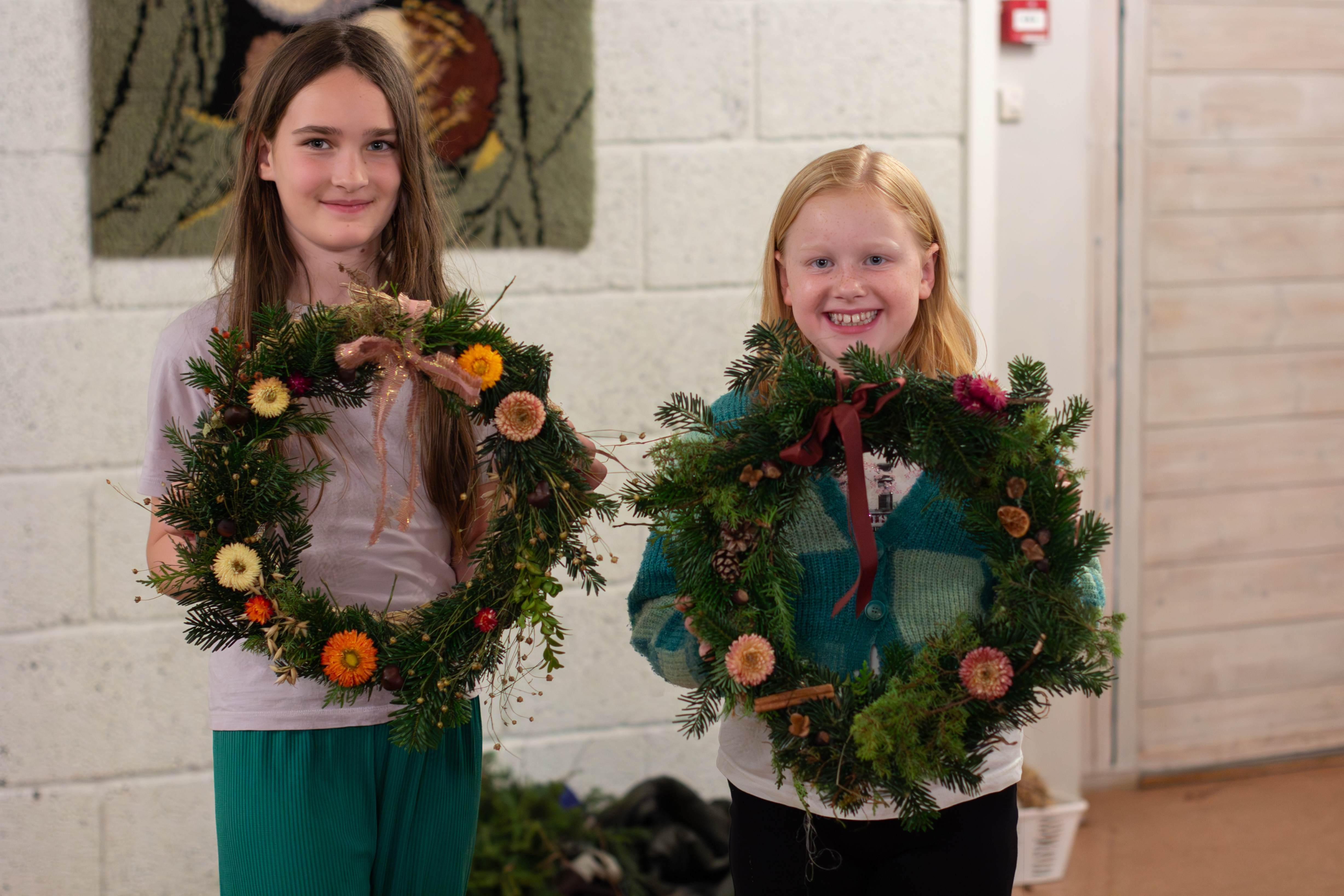To jenter holder opp hver sin grønne krans og smiler