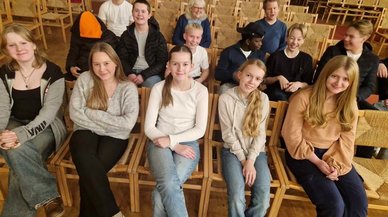 Ungdommer sitter på stolradene i kirken, de smiler til kameraet