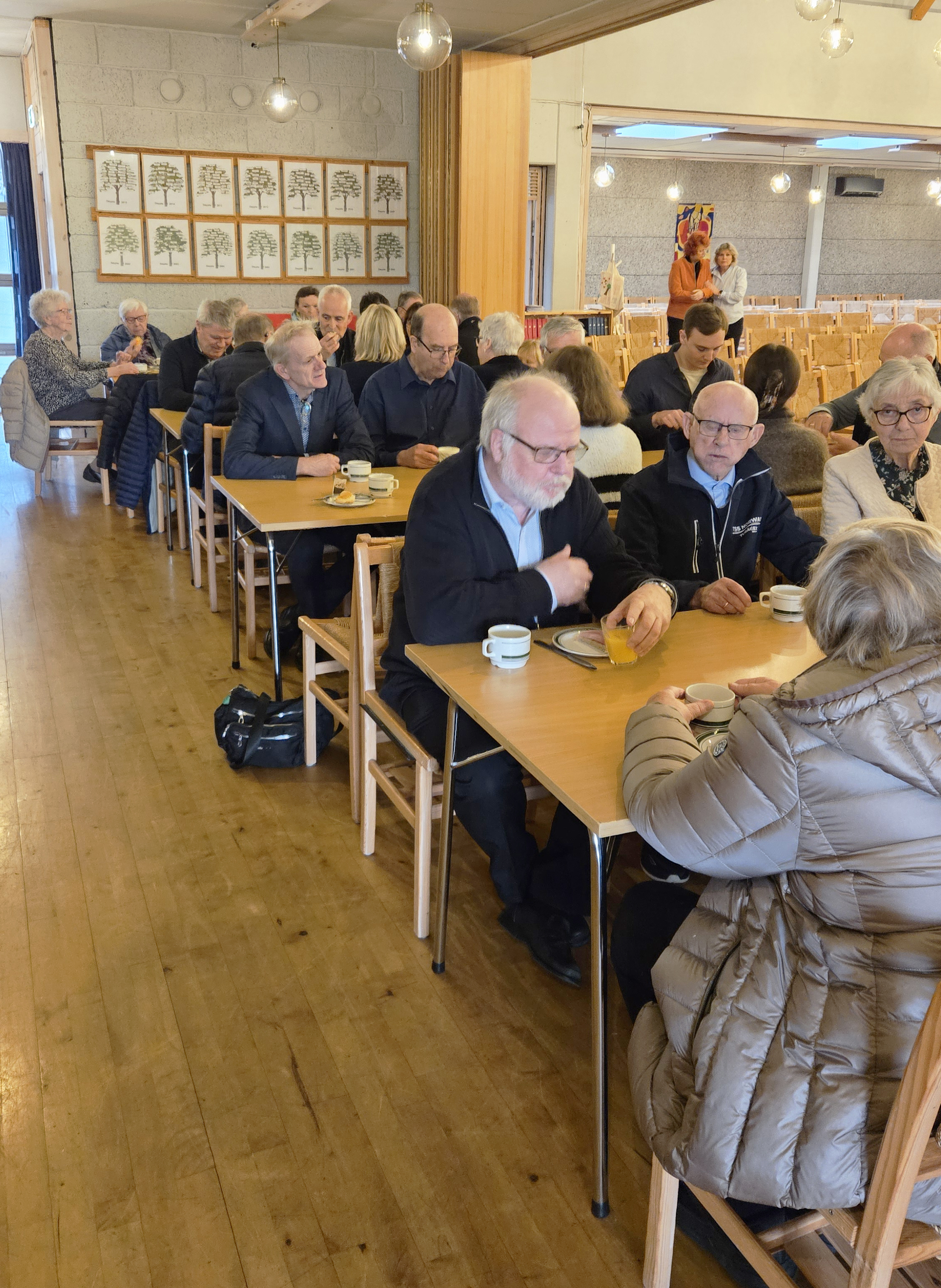 Mennesker sitter ved flere bord inne i salen og spiser kveldsmat og prater sammen