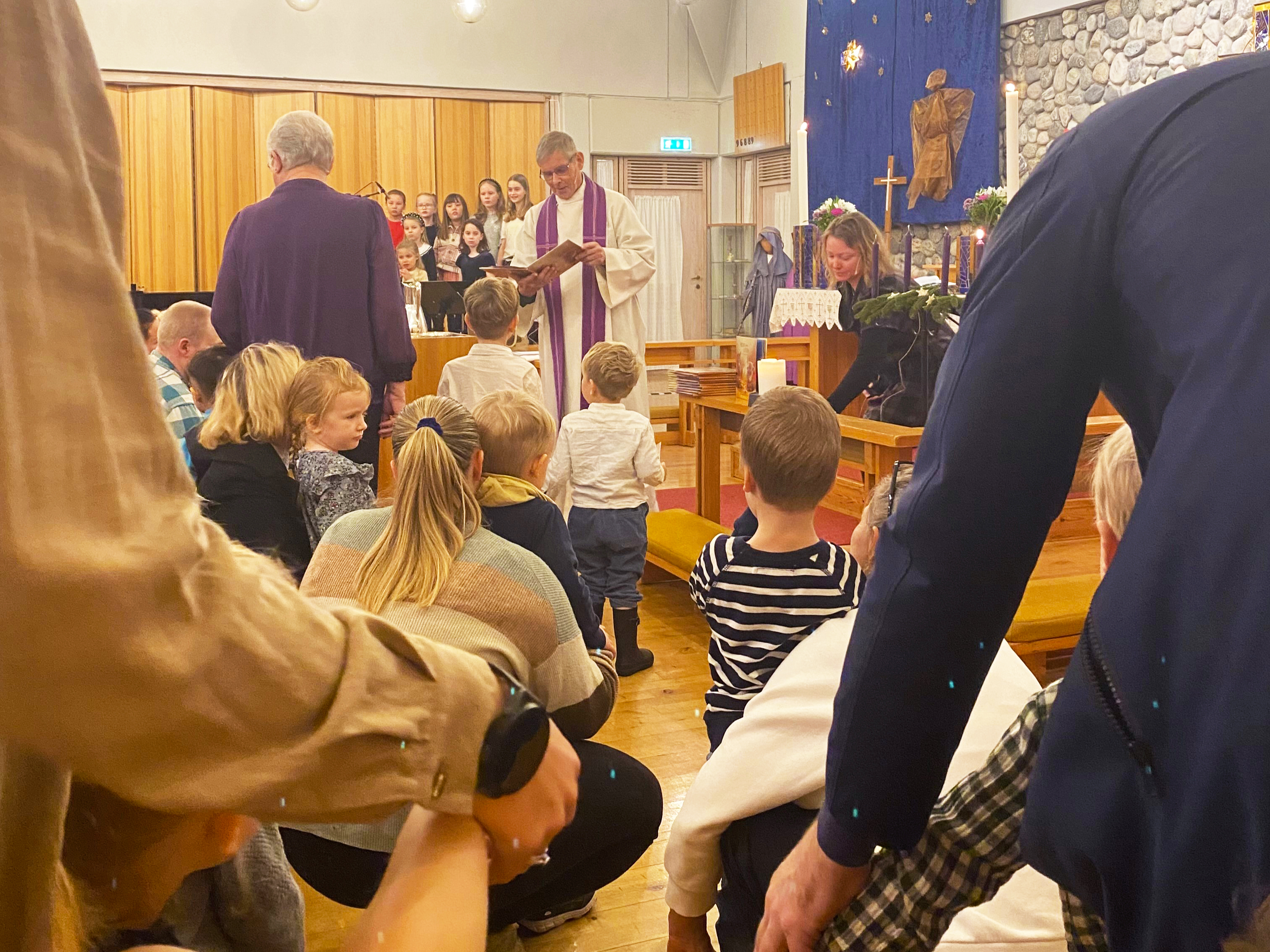 Prest og pedagog står framme i kyrkja og deler ut bøker til tre-åringer som er med foreldre og besteforeldre