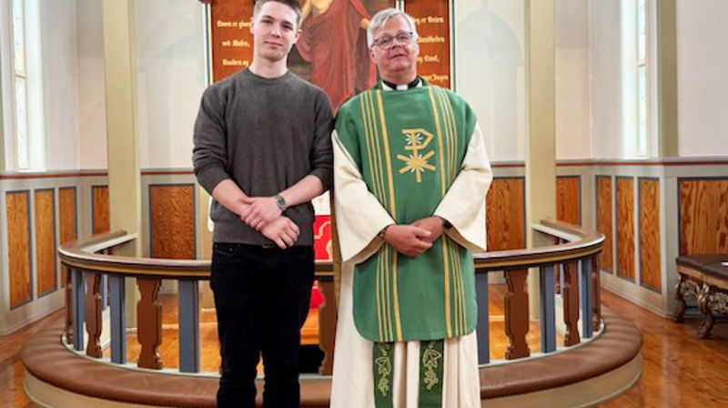 En ungdom og  en mannlig prest står ved siden av hverandre fremme i kirken og ser inn i kameraet