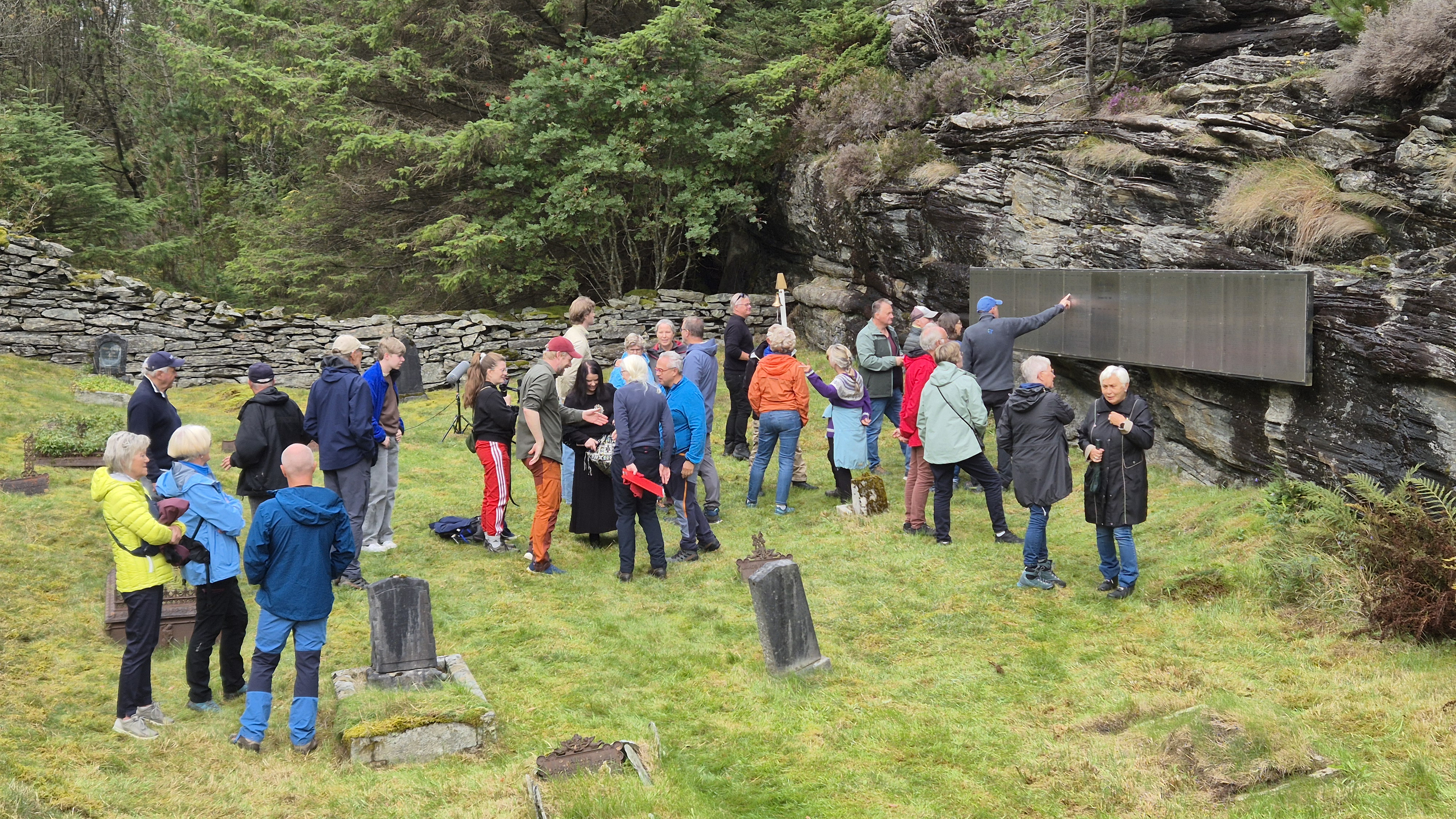 Mennesker på den gamle gravplassen, noen står og ser på navneskiltene som henger på fjellveggen
