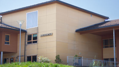 Et gult bygg med gress framfor. på et treskilt på veggen står det gravert inn "Sundheimen"