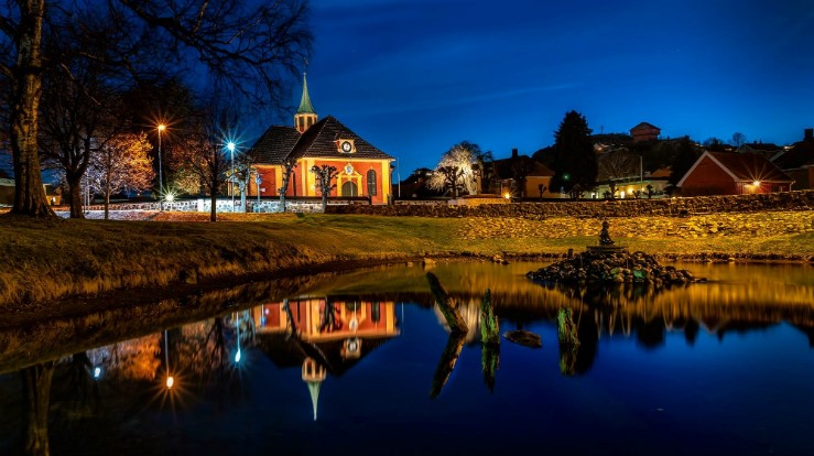 Stemningsfullt og vakkert bilde av Stavern kirke i Larvik kommune, Vestfold fylke og Tunsberg bispedømme. Legg merke til hvor fint fotografen har brukt trær, himmelen og vannet for å ramme inn kirken. Foto: John Nilsen