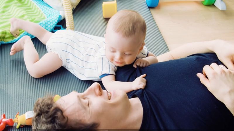 En far ligger på gulvet mens han ser på en baby som ligger ved siden av.
